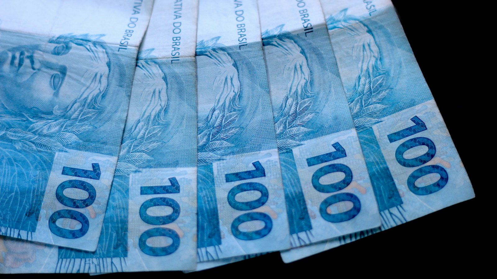 Cédulas de 100 reais lado a lado sobre fundo escuro